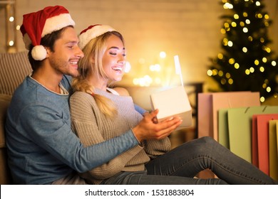 Xmas Magic. Loving Couple Opening Christmas Gift Box In Front Of Christmas Tree