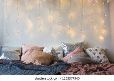 Xmas In Morning Bedroom. Double Bed In Christmas Interior On White Wall Background With Cozy Lights. Gift Box On Bed. Many Pillows On Bed