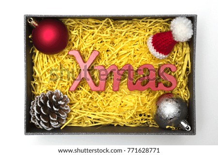 X-mas text and fur hat, ball, pine cone in black gift box with yellow packaging material