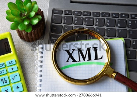 XML (Extensible Markup Language) acronym in notebook under magnifying glass with laptop and calculator in background