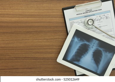 X-ray Lung Image In Tablet Computer And Stethoscope With Medical Document On Desk Of Doctor Radiologist. Top View.