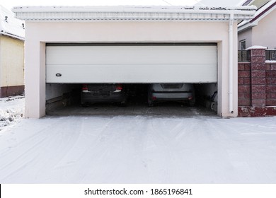 Xterior Of A  Garage Attached To A House. Garage With Two Cars Inside In Winter. Semi-open Sectional  Doors