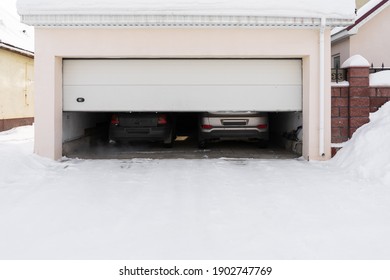 Xterior Of A Garage Attached To A House. Garage With Two Cars Inside In Winter. Semi-open Sectional Doors