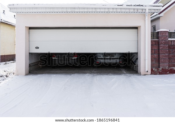 xterior of a  garage\
attached to a house. garage with two cars inside in winter.\
semi-open sectional \
doors