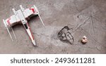 X-Wing star ship and BB-8 droid robot toy model on cracked abstract cement floor background