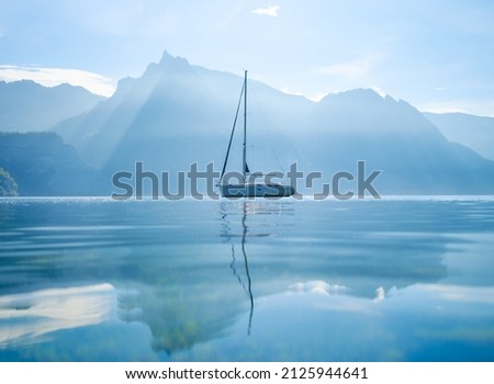 A yacht against the backdrop of the mountains in Switzerland. Calm water and bright sunny day. A popular place to travel and relax. 

