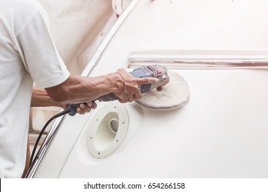 Yacht maintenance. A man polishing side of the white boat by grinder machine in the marina - Powered by Shutterstock