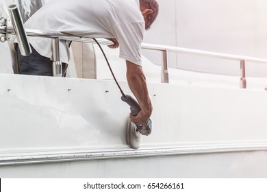 Yacht maintenance. A man polishing side of the white boat by grinder machine in the marina - Powered by Shutterstock