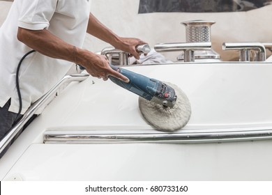 Yacht maintenance. A man polishing side of the white boat by grinder machine in the marina - Powered by Shutterstock