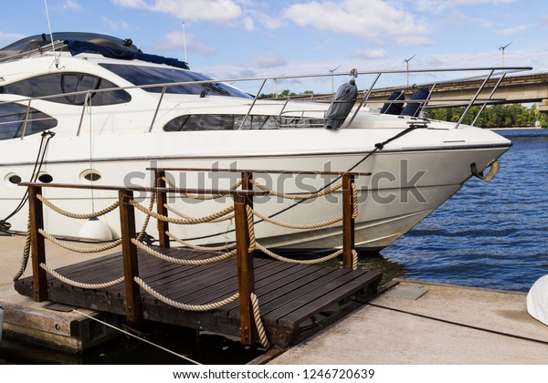 The yacht is moored at the pier of\
the river, near a wooden bridge. Part of the\
frame\

