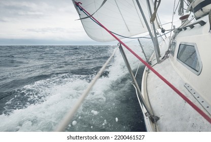 Yacht Sailing During The Storm. Close-up View From The Deck To The Bow, Mast, Sails. Dramatic Sky, Dark Clouds, Waves, Water Splashes. North Sea, Norway. Epic Seascape. Rough Weather