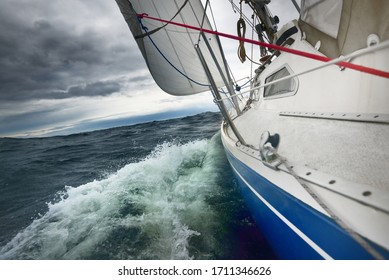 Yacht Sailing In A Thunderstorm On A Rainy Day. Close-up View From The Deck To The Bow, Mast And Sails. Dramatic Stormy Sky, Dark Clouds. Waves And Water Splashes. Rough Weather. Baltic Sea, Sweden