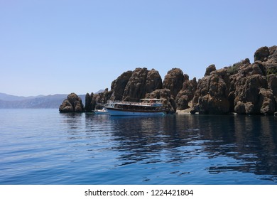 Yacht and ship are in blue water near rocky sea coast at sunny summer day