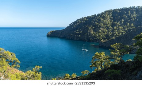 A yacht in the stunning Turkish Mediterranean coastline in Antalya, inside a blue sea, surrounded by lush green forests, and rugged rocky shores, attracting tourists every summer. - Powered by Shutterstock