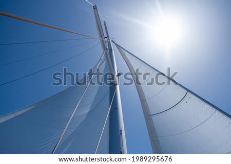 Yacht wind filled sails on clear blue sky background. Sailing with the wind at open sea ocean, summer vacations concept. Looking up at the sky, sun shining, sunbeams on boat rigging, Low angle view