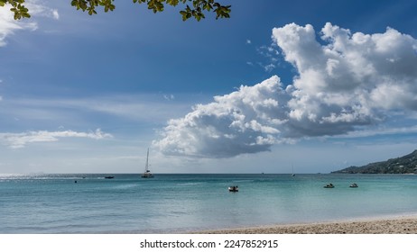 Yachts and boats are visible on the calm turquoise water of the ocean. Picturesque clouds in the blue sky. Branches and green leaves over a sandy beach. Seychelles. Mahe. Beau Vallon - Shutterstock ID 2247852915