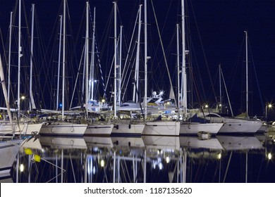 Yachts in the port of the Greek island. Night, the reflection of ships and masts in dark blue water.