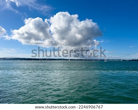 Yachts sailing on the green colored sea with a huge cumulonimbus cloud. Beyond the sea, towns and mountains are clearly seen.