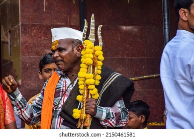 Yadgir,India- December 22nd 2019; Stock photo of Indian priest, wearing casual cloths, saffron color scarf,white cap and holding trishul decorated with marigold flower garland in Indian village temple