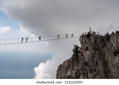 YALTA, RUSSIA - AUGUST 25, 2021: Tourists cross the cliff in the Ai-Petri mountains in the Crimea on a suspension bridge