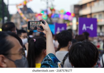 Yamagata City, Yamagata, Japan - August 7, 2022: A woman records a parade with her cell phone during a summer festival. 