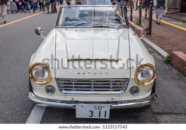 YAMAGUCHI, JAPAN - APRIL 8, 2018: A close up,\
front view of a vintage, classic, cream colored, Nissan Datsun\
Fairlady convertible sports car with distinctive shiny gold\
headlights and a chrome\
bumper.