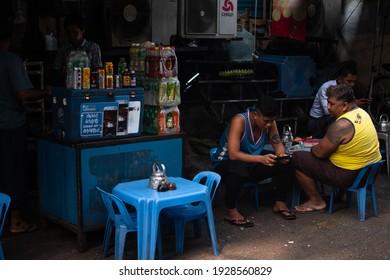 YANGON, MYANMAR - JANUARY 1 2020: A Few Burmese People Sits On Plastic Chairs And Enjoys Some Rest At A Food And Drink Stall In Central City