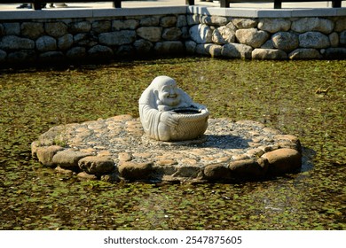 Yangyang County, South Korea - November 3rd, 2024: A cheerful Laughing Buddha statue rests at the center of a reflecting pond at Naksansa Temple, surrounded by lily pads and tranquil water. - Powered by Shutterstock