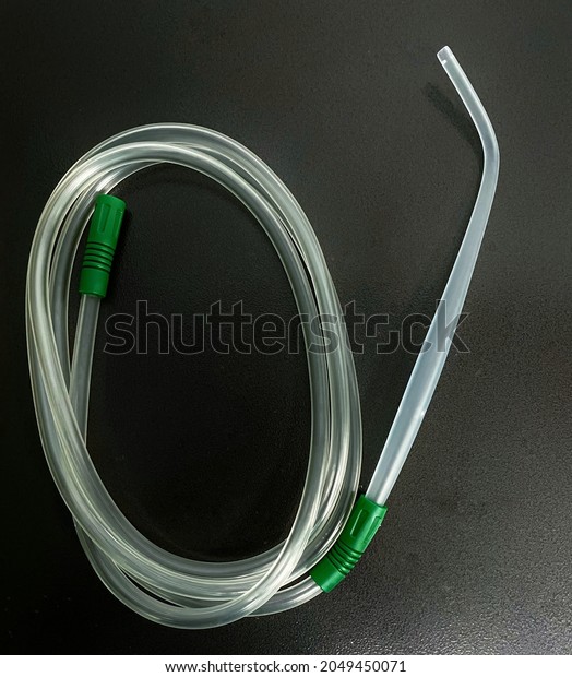 A Yankauer suction set with suction tubing\
placed on a dark background 