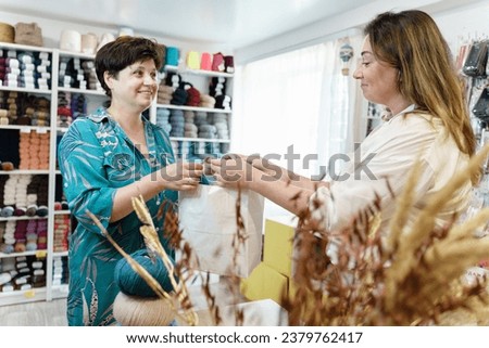 Yarn shop. Friendly seller of yarn giving shopping bag to a satisfied female customer. Yarn store owner handing over the shopping bag to a woman buyer at checkout