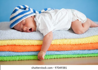 Yawning sleeping baby on colorful towels stack