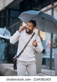 Yeah it just started raining. Cropped shot of a handsome young businessman making a phonecall while walking through the city with an umbrella.