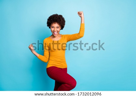 Yeah we win. Excited crazy ecstatic afro american girl enjoy lottery luck raise fists scream yeah wear stylish trendy sweater isolated over blue color background