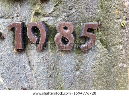 The year 1985 cast in metal and affixed to a stone. Produced that year