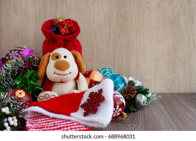 Year of the dog. A toy dog is holding a red bag with gifts. A knitted scarf, snowflake, Christmas tree urchase make a New Year mood. Dog as a symbol of the new year by the zodiac.