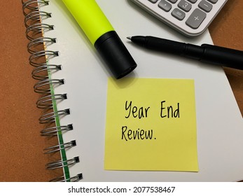 Year end review text on sticky note pad with calculator and pen background