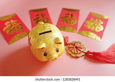 Year of the Pig, Chinese Lunar New Year celebrations theme golden piggy bank, red envelope with blessing word means happiness or good fortune, hanging decoration on pink background. (selective focus)