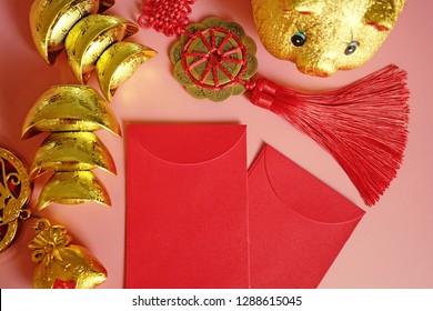 Year of the Pig Chinese Lunar New Year celebrations theme blank red envelopes, golden piggy bank, traditional Chinese ancient gold bullion nugget flat lay on pink background / top view, space for text