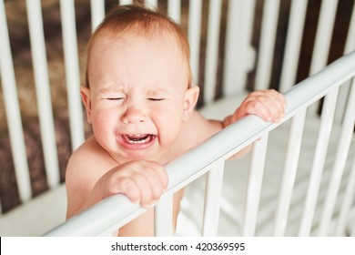 A Year-old Child Is Crying In The Crib And Holds Onto The Side Of The Bed