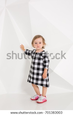 Year-old child in plaid dress standing near white wall in studio