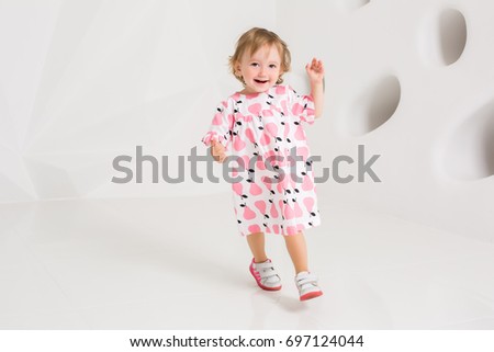 Year-old child in summer dress standing near white wall in studio