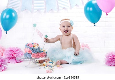 year-old girl in a blue skirt with a bandage on his head sits near a cream cake pink and blue