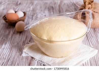 Yeast dough in a glass bowl under cling film on wooden table. Selective focus - Powered by Shutterstock