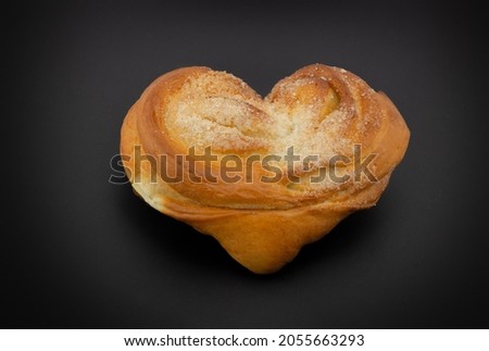 Yeast sweet bun in the shape of a heart or plyushka Moskovskaya isolated on black background. Tasty and beautiful pastry bun. Russian authentically style