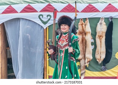 Yekaterinburg, Russia - June 25, 2022: Portrait Of Beautiful Asian Woman In Traditional Festive Bashkir Clothes, Fur Hat, Guarding Entrance To Yurt With Bow And Arrow At Sabantuy Folk Festival.