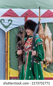 Yekaterinburg, Russia - June 25, 2022: Beautiful Asian Woman In Traditional Festive Bashkir Clothes, Fur Hat, With Bow And Arrow Over Background Of Yurt And Fox Skins At Sabantuy Folk Festival.