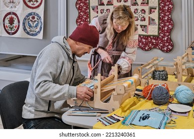 Yekaterinburg, Russia - May 2, 2022: Asian Man, Weaving Small Rug With Pattern At Masterclass On Weaving. Caucasian Woman In Russian Folk Dress Teaching How To Weave On Manual Table Loom.