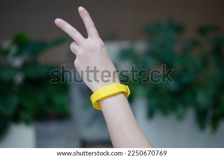 Yellow access bracelet with a chip. Contactless silicone key pass. Waterproof key bracelet for hotel client. Functional gadget RFID wristband on female hand, focus on the strap.