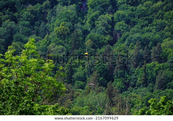 Yellow aerial tram runs\
along a cableway over a green forest in summer. Popular tourist\
destination in Sigulda, holidays in Latvia. Sigulda, Latvia - 12\
Jun 2022.
