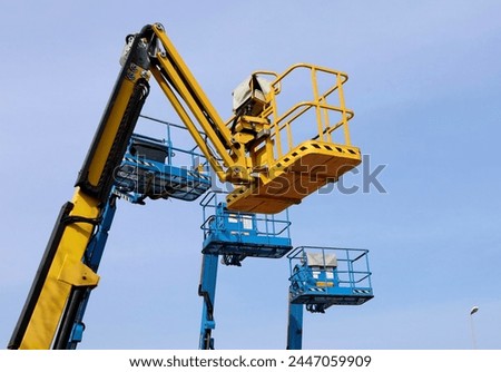 Yellow aerial working platform of cherry picker in front of other three blue. Slightly overcast sky.